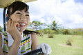 ゴルフカートに乗って電話をする日本人女性ゴルファー