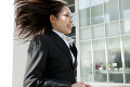 髪の毛をなびかせてオフィス街を走るスーツ姿の女性