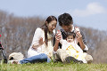 公園の芝生に腰掛ける若い夫婦と赤ちゃん