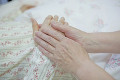 ベッドで横になるシニア女性の手を握るシニア女性