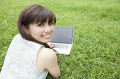 公園の芝生でパソコンをする若い女性