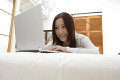 ベッドで横になりながらノートパソコンに向かう日本人女性