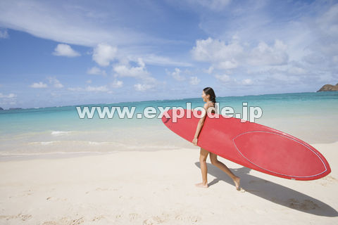 サーフボードを持って海辺を歩く日本人女性