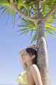 椰子の木に寄りかかりながら空を見上げる水着女性