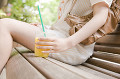 オレンジシュースを片手に持って街中のベンチに座っている女性