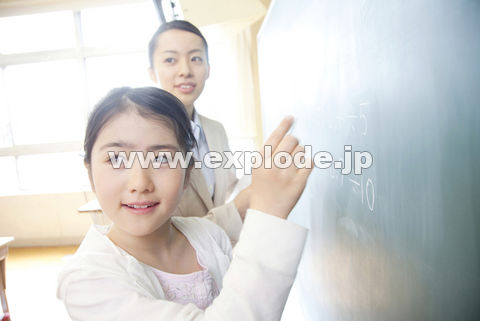 黒板の問題を解く小学生女子と横に立つ女性教師