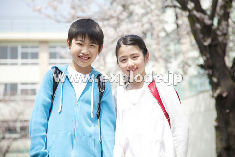 校庭の桜の下で微笑む小学生男女