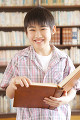 図書室で本を持って微笑む小学生男子