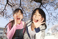 桜の下で叫ぶ笑顔の小学生女子2人