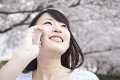 桜の下で電話をする笑顔の女性
