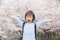 桜の下で手を広げ微笑む小学生男子