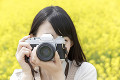 菜の花畑でカメラを構える女性