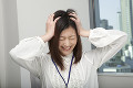 職場で頭を抱えて顔をしかめる若い女性