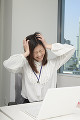 職場で頭を抱えて顔をしかめる若い女性