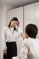 職場で頭に手を当て顔をしかめる若い女性