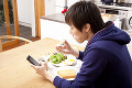 携帯電話を見ながらトーストを食べる男性