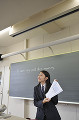 黒板の前で教科書を見せる女子高校生