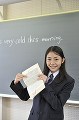 黒板の前で辞書を見せる女子高校生