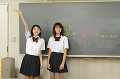 黒板の前に立つ女子高校生二人