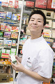 商品棚の前で薬を持つ笑顔の男性登録販売者