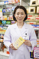 商品棚の前で薬を持つ笑顔の女性薬剤師