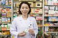 商品棚の前で薬を持つ笑顔の女性薬剤師